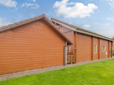An exterior view of a wooden house with a grassy lawn at Jamaal Lodge in South Broomhill near Amble