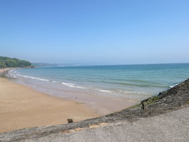 A sandy beach with waves and some people near the water and a forested area in the distance at Potters Barn in Begelly near Kilgetty