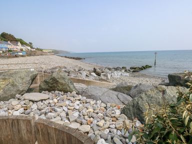 A pebble beach with large rocks and houses along the shoreline at Potters Barn in Begelly near Kilgetty