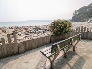 A bench on a paved area with stones and ocean in the background at Potters Barn in Begelly near Kilgetty