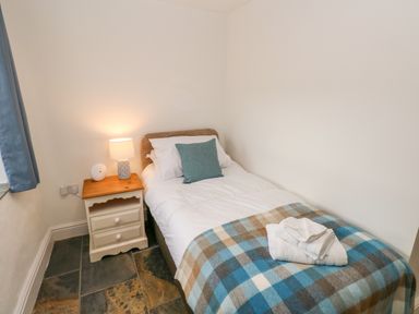 A bedroom with a single bed bedside table with a lamp and folded towels on the bed at Potters Barn in Begelly near Kilgetty