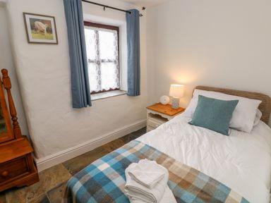 A bedroom with a single bed a bedside table with a lamp a window with blue curtains and a wooden dresser at Potters Barn in Begelly near Kilgetty