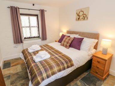 A bedroom with a double bed two bedside tables with lamps a window with curtains and a blanket on the bed at Potters Barn in Begelly near Kilgetty