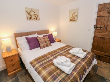 A bedroom with a bed with plaid blanket and pillows two bedside tables with lamps and wooden door at Potters Barn Begelly near Kilgetty