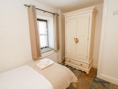 A bedroom with a bed and folded towels beside a window and a white wardrobe at Potters Barn in Begelly near Kilgetty