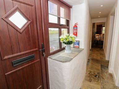 A hallway with a wooden front door a window with a flower vase on the sill and a fire extinguisher at Potters Barn in Begelly near Kilgetty