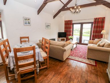 A living room with two sofas a dining table and chairs wooden floor and red curtains at Potters Barn in Begelly near Kilgetty