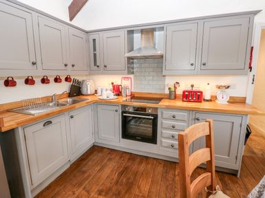 A kitchen with gray cabinets wooden countertop red mugs and toaster with stainless steel oven and wooden floor at Potters Barn in Begelly near Kilgetty