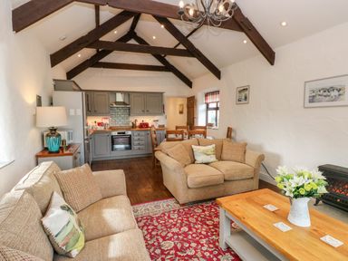 A living room with beige sofas wooden beams kitchen and dining area at Potters Barn in Begelly near Kilgetty