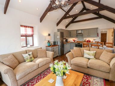 A living room with two beige sofas and a wooden coffee table with flowers next to a kitchen and dining area at Potters Barn in Begelly near Kilgetty