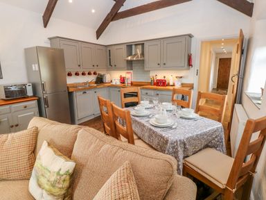 A kitchen and dining area with wooden chairs a table set with dishes and a sofa in Potters Barn Begelly near Kilgetty