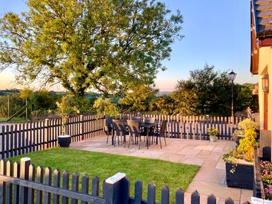 An outdoor patio area with a table and six chairs surrounded by a wooden picket fence and trees at Potters Barn in Begelly near Kilgetty