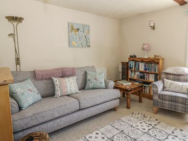 A living room with a gray sofa and cushions a wooden coffee table a wooden bookshelf an armchair and a floor lamp at Megs Cottage in Norwich