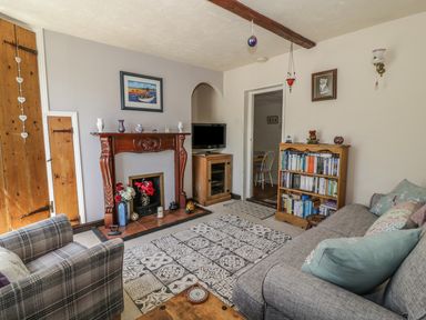 A living room with a wooden fireplace mantel a TV on a wooden cabinet a bookshelf a sofa with cushions and an armchair at Megs Cottage in Norwich