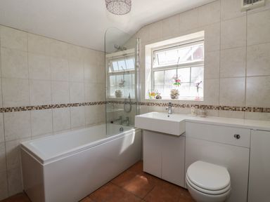 A bathroom with a bathtub shower combination a sink and toilet under a window at Megs Cottage in Norwich