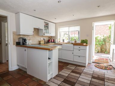 A kitchen with white cabinets wooden countertops a window and an open door to a patio at Megs Cottage in Norwich