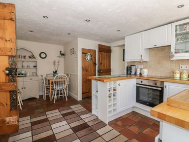 A kitchen with white cabinets wooden countertops a dining table with chairs a wooden door and a patterned rug at Megs Cottage in Norwich