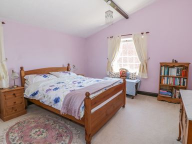A bedroom with a wooden bed a floral bedspread a small bookshelf and a window seat at Megs Cottage in Norwich