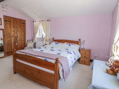 A bedroom with a wooden bed, floral bedding, wooden wardrobes, a bedside table with a lamp, and a small sofa with cushions and a teddy bear at Megs Cottage in Norwich