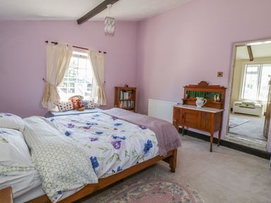 A bedroom with a bed a wooden cabinet a window with curtains and a bookshelf at Megs Cottage in Norwich