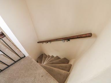 Carpeted spiral staircase with wooden handrail and metal safety gate at the top at Megs Cottage Norwich