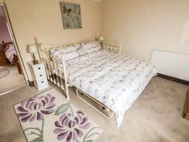 A bedroom with a floral bedspread on a metal bed frame two lamps on bedside tables a floral rug and a painting on the wall at Megs Cottage in Norwich