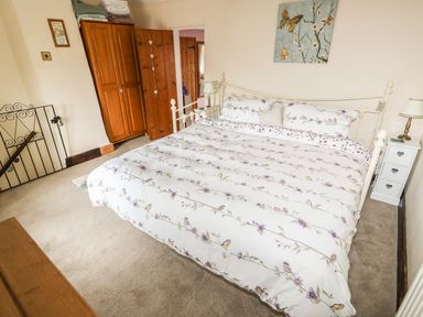A bedroom with a bed with floral bedding a wooden wardrobe bedside table with a lamp and a painting on the wall at Megs Cottage Norwich