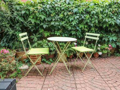 A garden patio with two chairs and a round table surrounded by potted plants and greenery at Megs Cottage in Norwich
