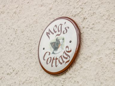 A circular sign on a textured wall with the text Megs Cottage and an illustration of a dog at Megs Cottage in Norwich