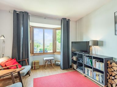 A living room with chairs and a stool near a window and a television on a shelving unit at Gorwel in Llan Ffestiniog near Blaenau Ffestiniog