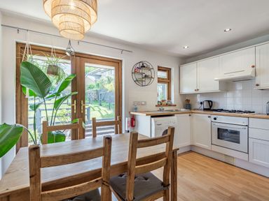 A kitchen with wooden dining table and chairs plants hanging near glass doors and white cabinets at Gorwel in Llan Ffestiniog near Blaenau Ffestiniog