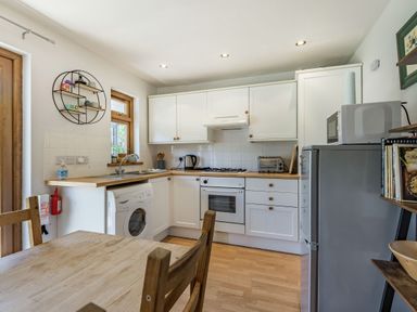 A kitchen with white cabinets a washing machine a refrigerator and a wooden dining table at Gorwel in Llan Ffestiniog near Blaenau Ffestiniog