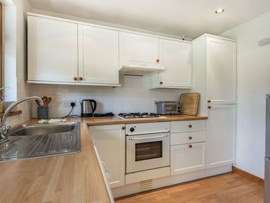 A kitchen with white cabinets wooden countertops a sink stove oven kettle toaster and cutting board at Gorwel in Llan Ffestiniog near Blaenau Ffestiniog