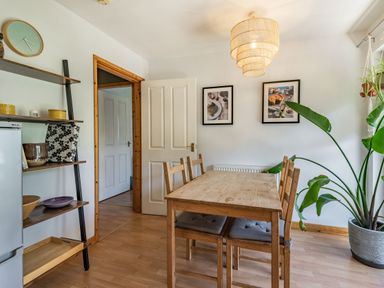A dining room with a wooden table and four chairs a tall green plant two framed pictures on the wall and shelves with kitchenware at Gorwel in Llan Ffestiniog near Blaenau Ffestiniog