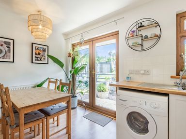 A dining area with wooden table and chairs next to glass patio doors and washing machine by kitchen sink at Gorwel in Llan Ffestiniog near Blaenau Ffestiniog