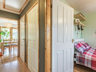 A hallway with three closed doors next to a bedroom with a bed with red and gray plaid bedding and wall shelves at Gorwel Llan Ffestiniog near Blaenau Ffestiniog