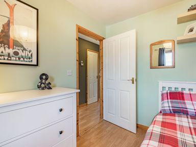 A bedroom with a white dresser a bed with red and gray plaid bedding a wall mirror and a door open to a hallway at Gorwel in Llan Ffestiniog near Blaenau Ffestiniog