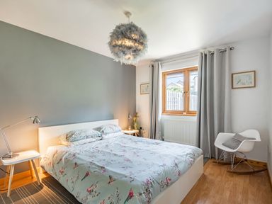 A bedroom with a bed two bedside tables with lamps a window with grey curtains and a rocking chair at Gorwel in Llan Ffestiniog near Blaenau Ffestiniog