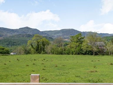 A grassy field with trees and hills in the background at Gorwel in Llan Ffestiniog near Blaenau Ffestiniog