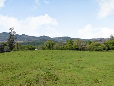 A grassy field with trees and hills in the background at Gorwel in Llan Ffestiniog near Blaenau Ffestiniog