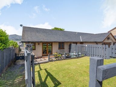 A single-story house with a gray roof and beige walls with a fenced grassy yard at Gorwel in Llan Ffestiniog near Blaenau Ffestiniog