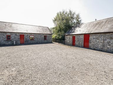 A gravel courtyard between two stone buildings with red doors and windows at The Visiting House in Gorteen near Dunmore County Galway