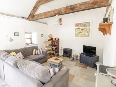 A living room with gray sofas wooden beams a rocking chair a small fireplace and a television at The Visiting House in Gorteen near Dunmore County Galway