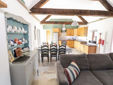 A kitchen and dining area with wooden cabinets a dining table with chairs and a gray sofa with a striped pillow at The Visiting House in Gorteen near Dunmore County Galway