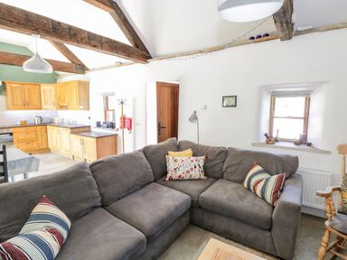An open living room and kitchen with a gray sectional sofa and wooden kitchen cabinets at The Visiting House in Gorteen near Dunmore County Galway