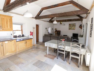 A combined kitchen and dining area with wooden cabinets, a dining table with chairs, and a living area with a sofa and television at The Visiting House in Gorteen near Dunmore County Galway