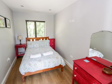 A bedroom with a bed two rolled towels a bedside table with lamp a chest of drawers with mirror and two framed pictures on the wall at The Visiting House in Gorteen near Dunmore County Galway