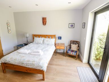 A bedroom with a wooden bed with white floral bedding a wooden side table and chairs next to a glass door at The Visiting House in Gorteen near Dunmore County Galway