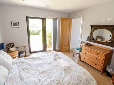 A bedroom with a bed linens dresser chairs and glass door at The Visiting House in Gorteen near Dunmore County Galway