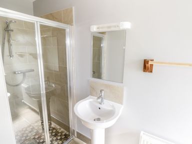 A bathroom with a glass shower enclosure a white pedestal sink a mirror and a wooden towel rack at The Visiting House in Gorteen near Dunmore County Galway